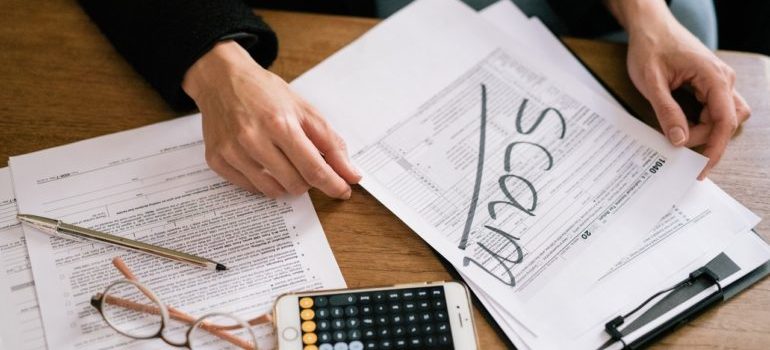 hands on the table and sign scam written on the documents, phone and pencils 