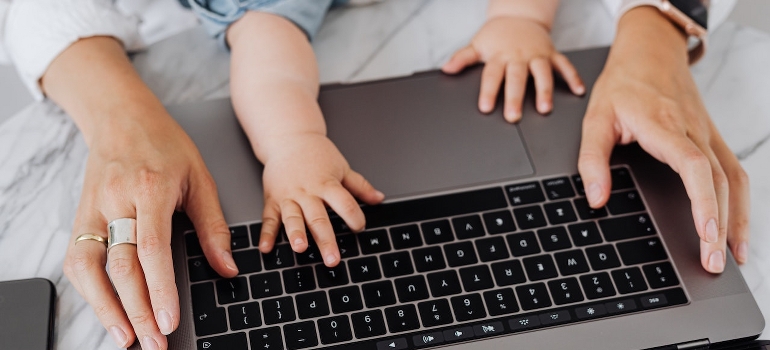 A woman holds her baby and using a laptop