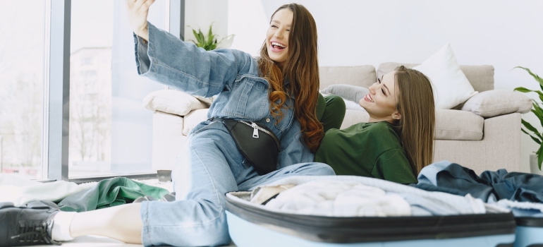 Two friends sitting on the floor and taking selfies.