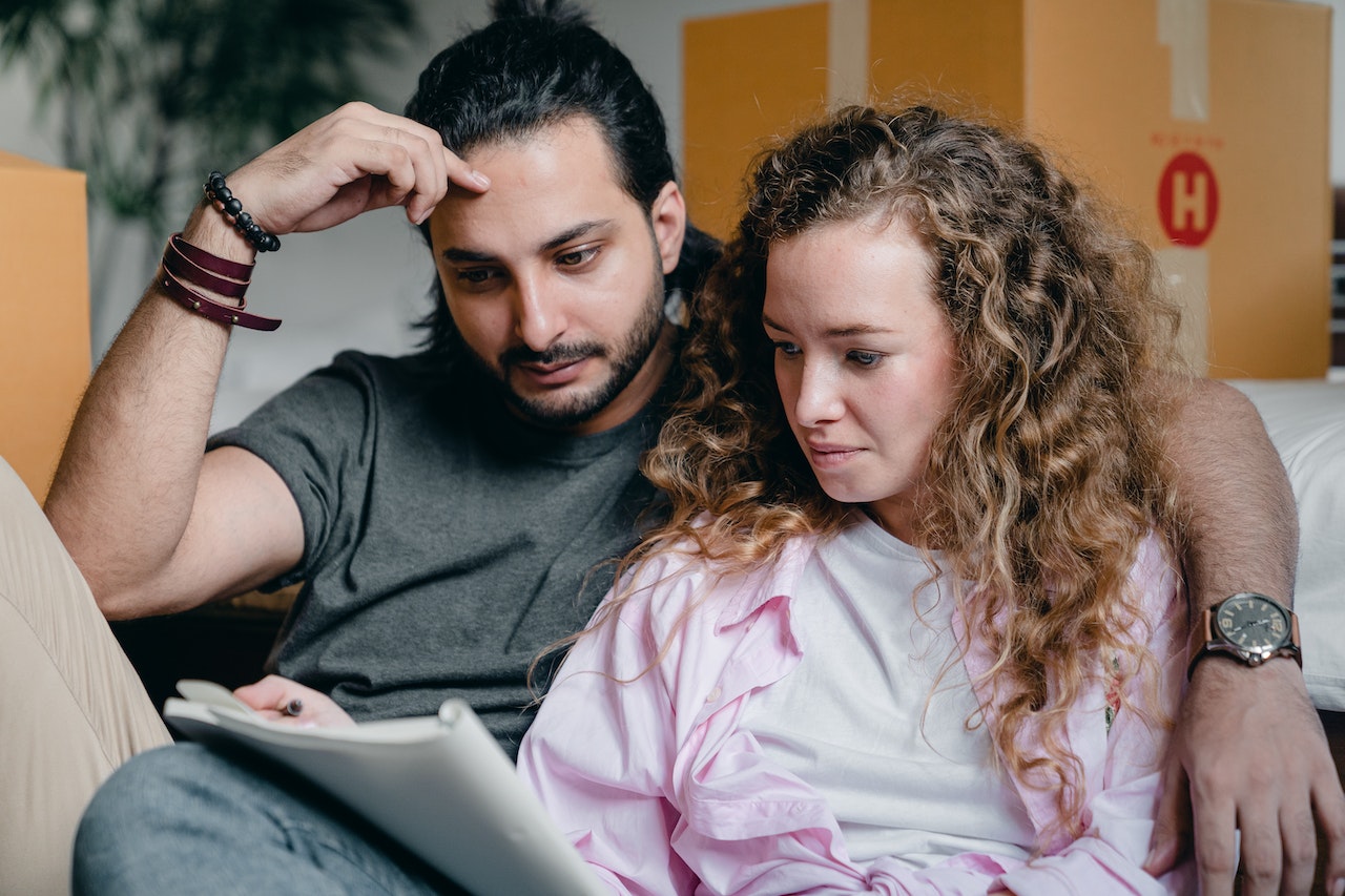 A couple is sitting next to boxes and looking at a notebook.