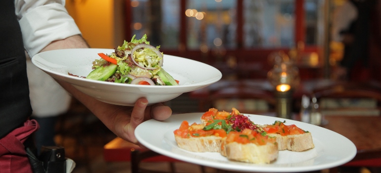 waiter carrying two plates in one of the restaurants you can go out for Thanksgiving dinner in Dallas–Fort Worth metroplex